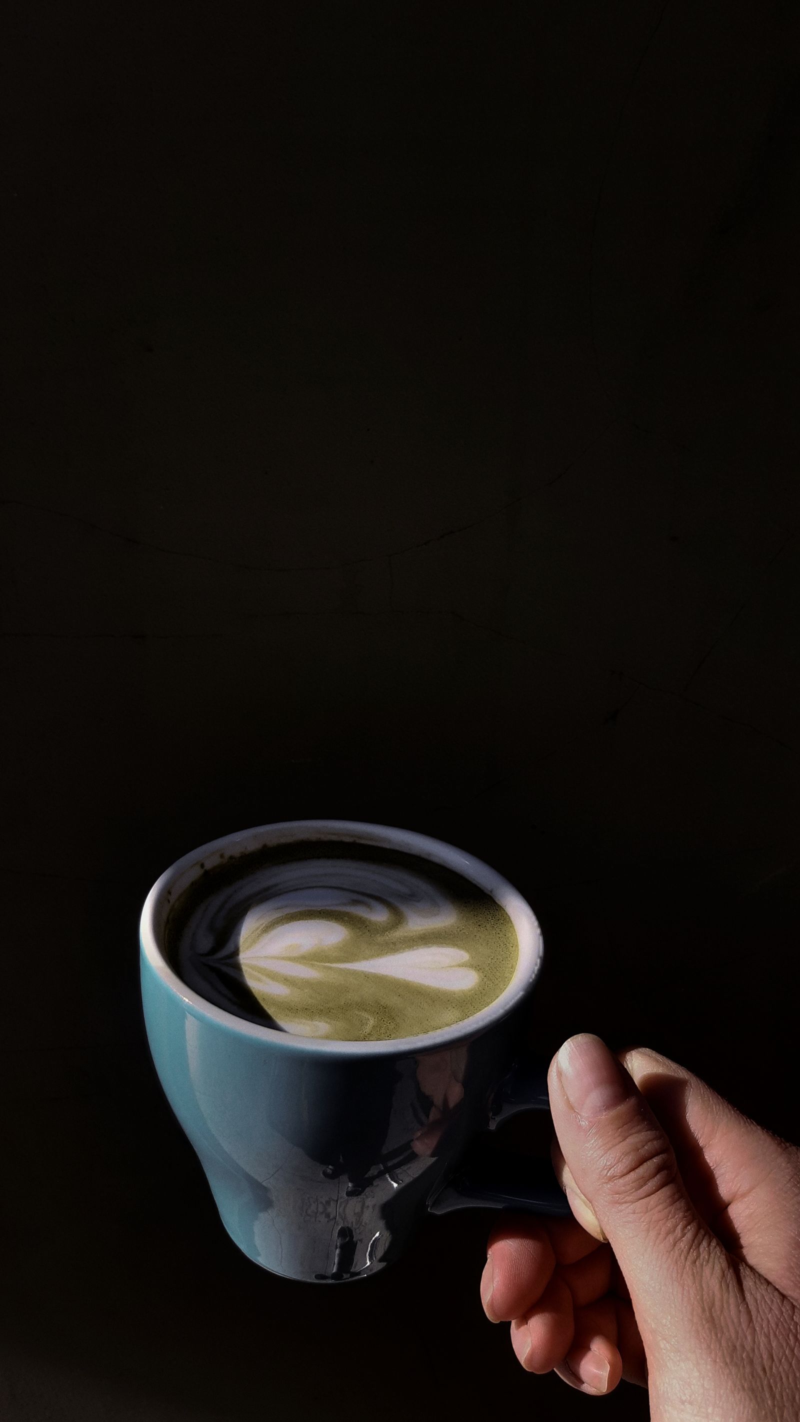 A hand holding a matcha latte against a near-black backdrop
